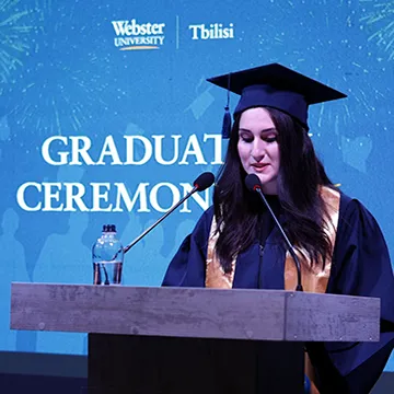 Graduate student speaking at the podium during the ceremony at Webster Tbilisi. 